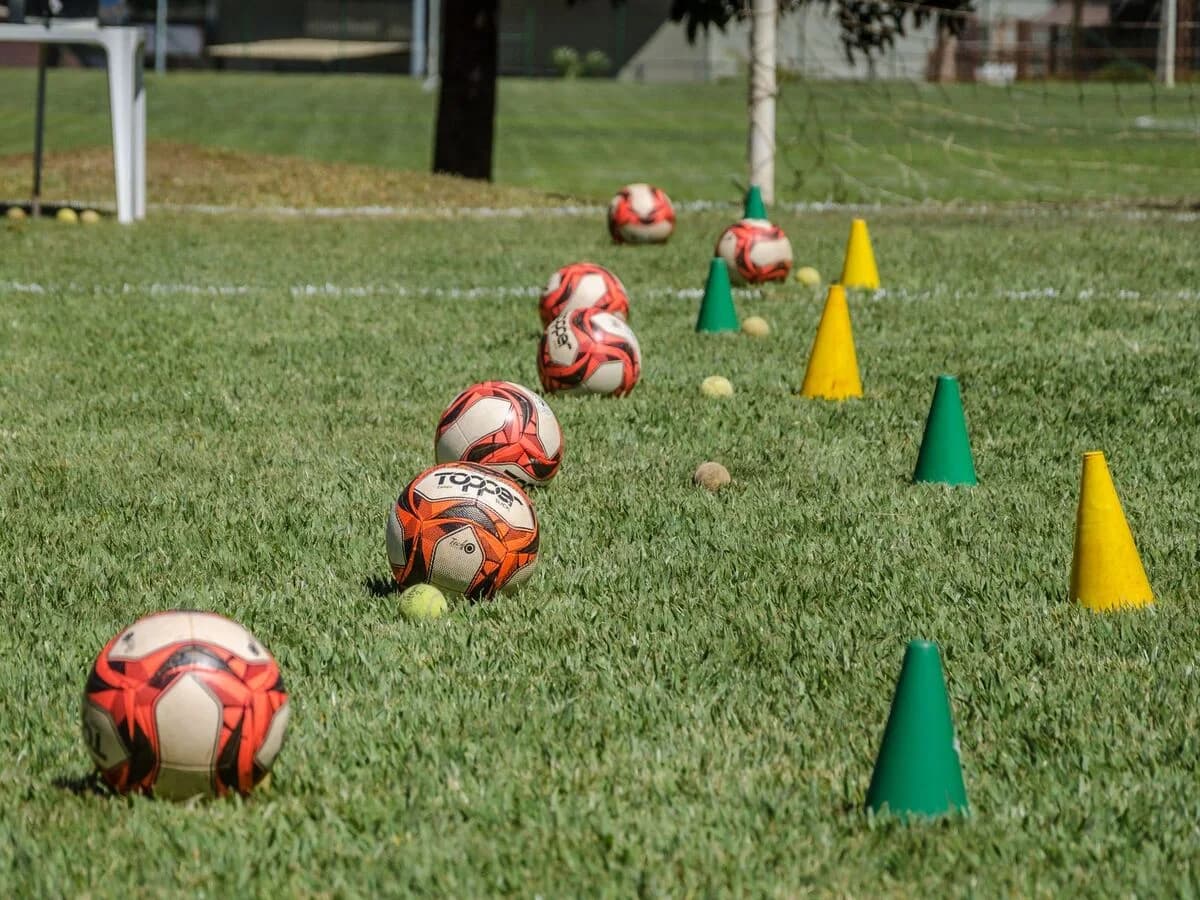 Cones de treino coloridos e bolas de futebol expostos em campo esportivo