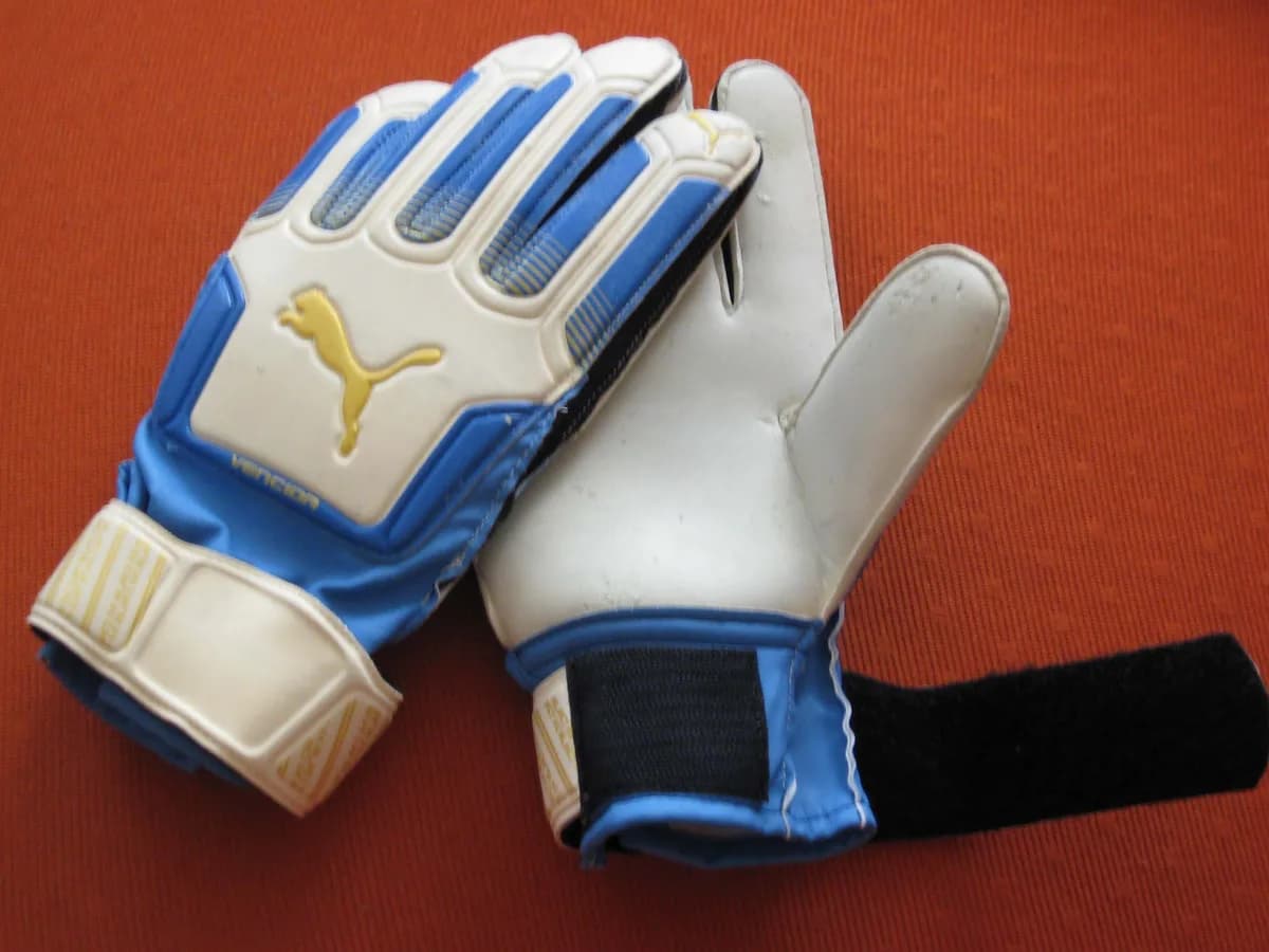 Par de luvas de goleiro azul e branca sobre uma superfície vermelha