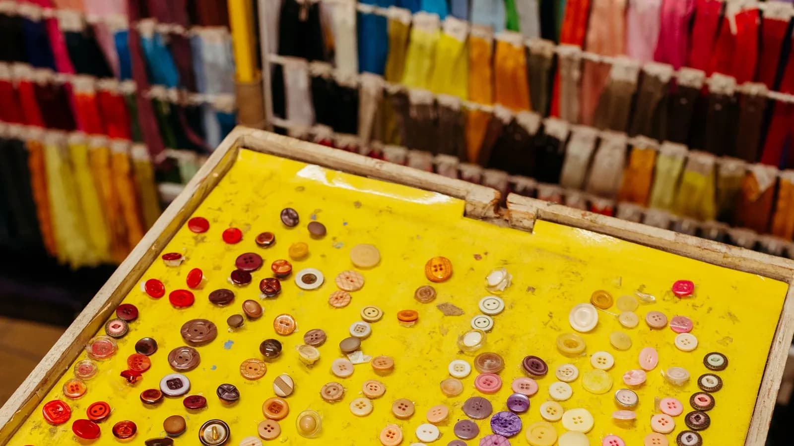 Interior de uma loja de aviamentos com cartela de botões e fileiras coloridas de fitas e linhas expostas