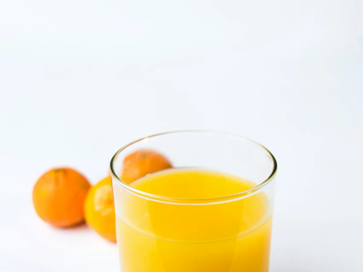Copo de suco de frutas com laranjas ao fundo, referência da família de sucos