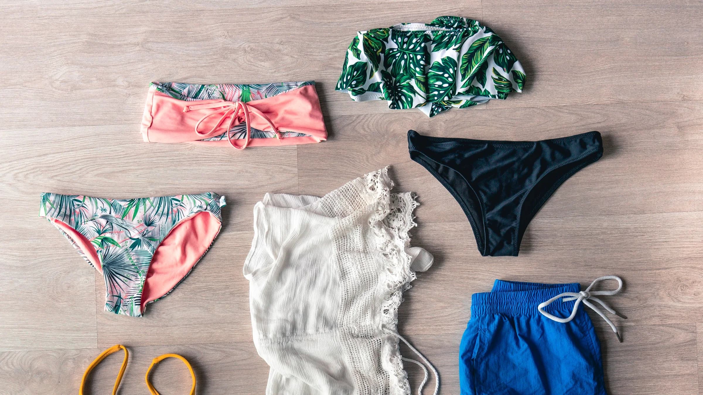 Biquínis, shorts de banho azul e saída de praia organizados em composição editorial