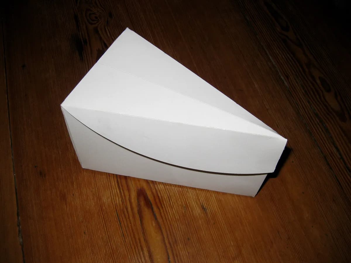 Caixa branca de papel para bolo dobrada sobre uma mesa