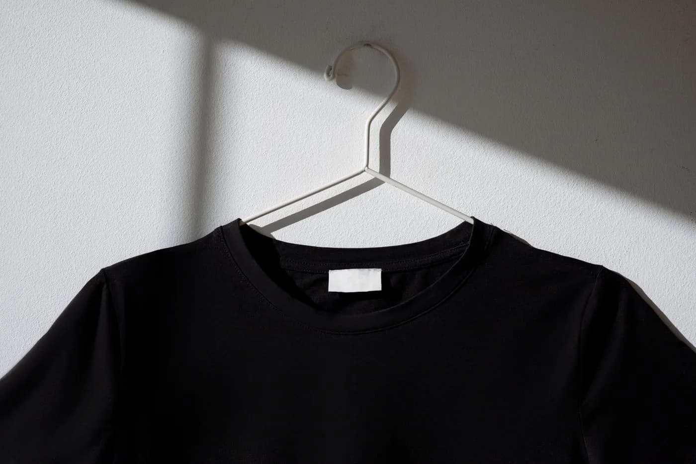 Camiseta básica preta em cabide sobre parede clara