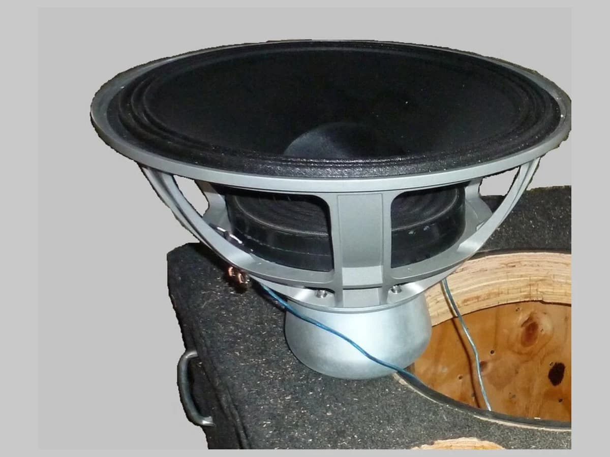 Subwoofer sem marca apoiado sobre uma caixa acústica revestida