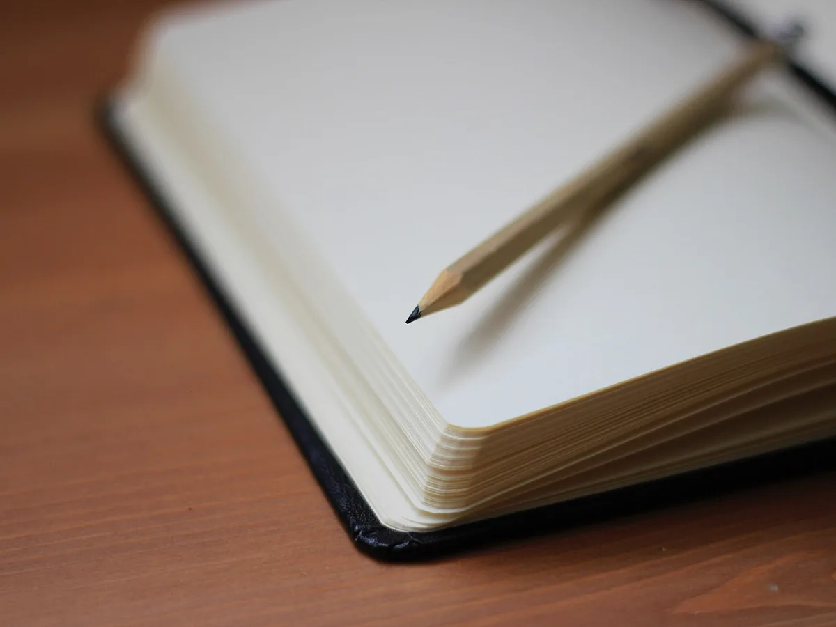 Caderno de capa escura aberto com lápis sobre mesa de madeira