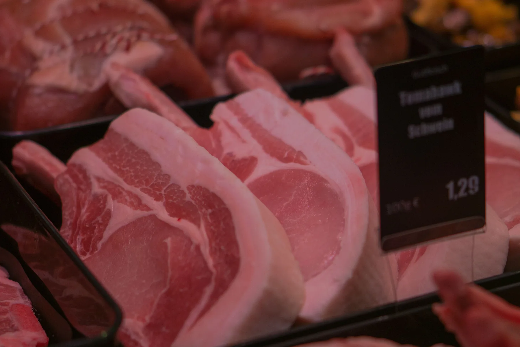 Cortes de carne suína crus organizados em bandejas de balcão refrigerado, sem marca ou letreiro legível
