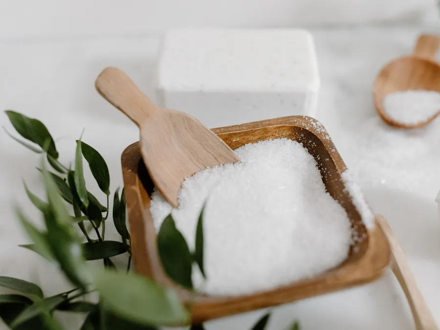 Sal branco em grãos em recipiente de madeira com uma pá
