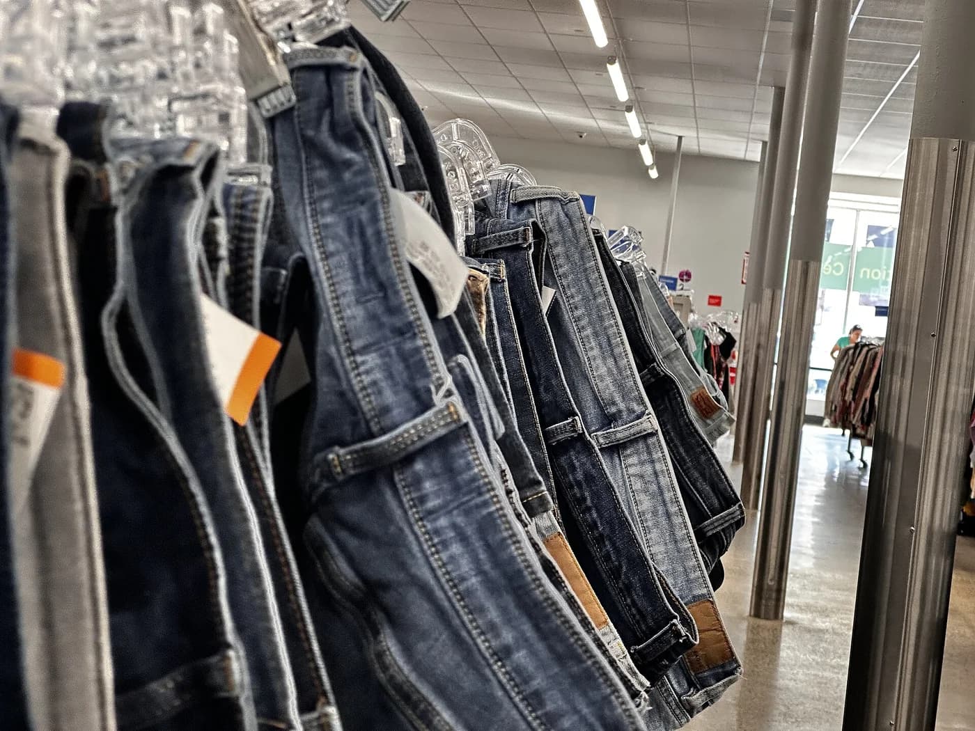 Arara com várias peças jeans usadas penduradas lado a lado em uma loja de segunda mão