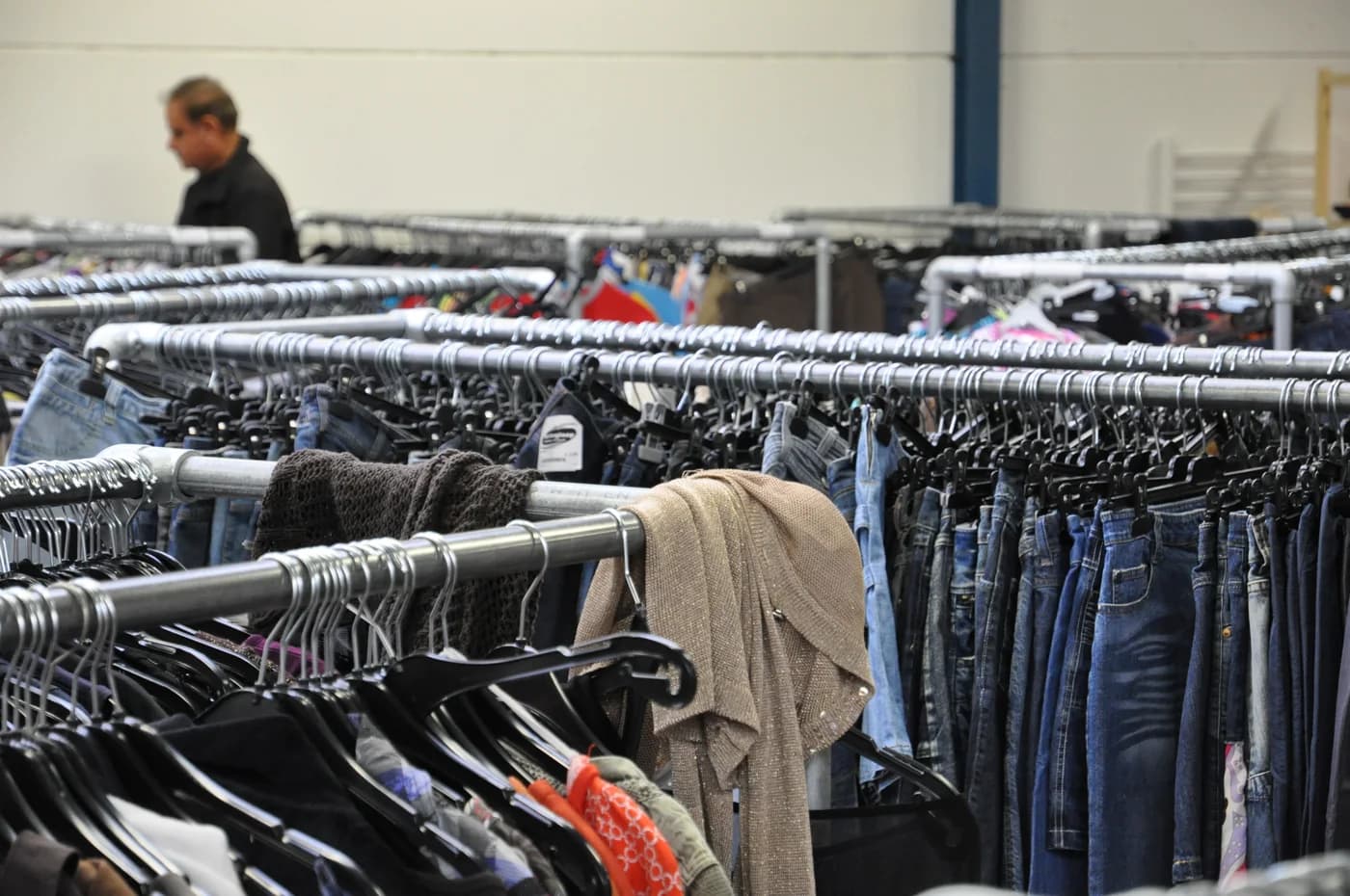 Araras cheias de roupas usadas dentro de uma loja de segunda mão, sem texto ou marca em destaque