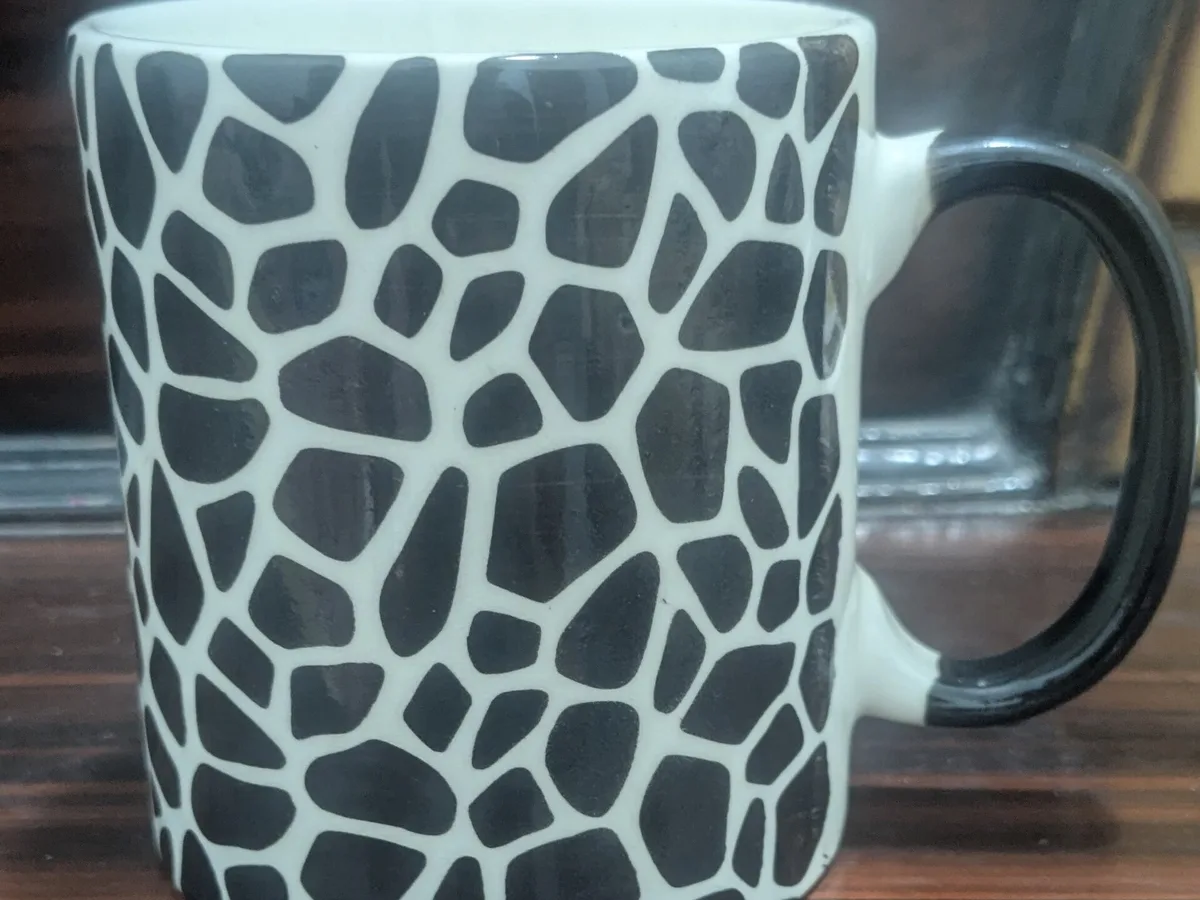 Caneca cerâmica decorada com padrão preto, fotografada de frente