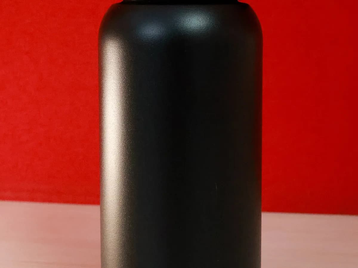 Squeeze metálico preto sem marca visível em fundo vermelho