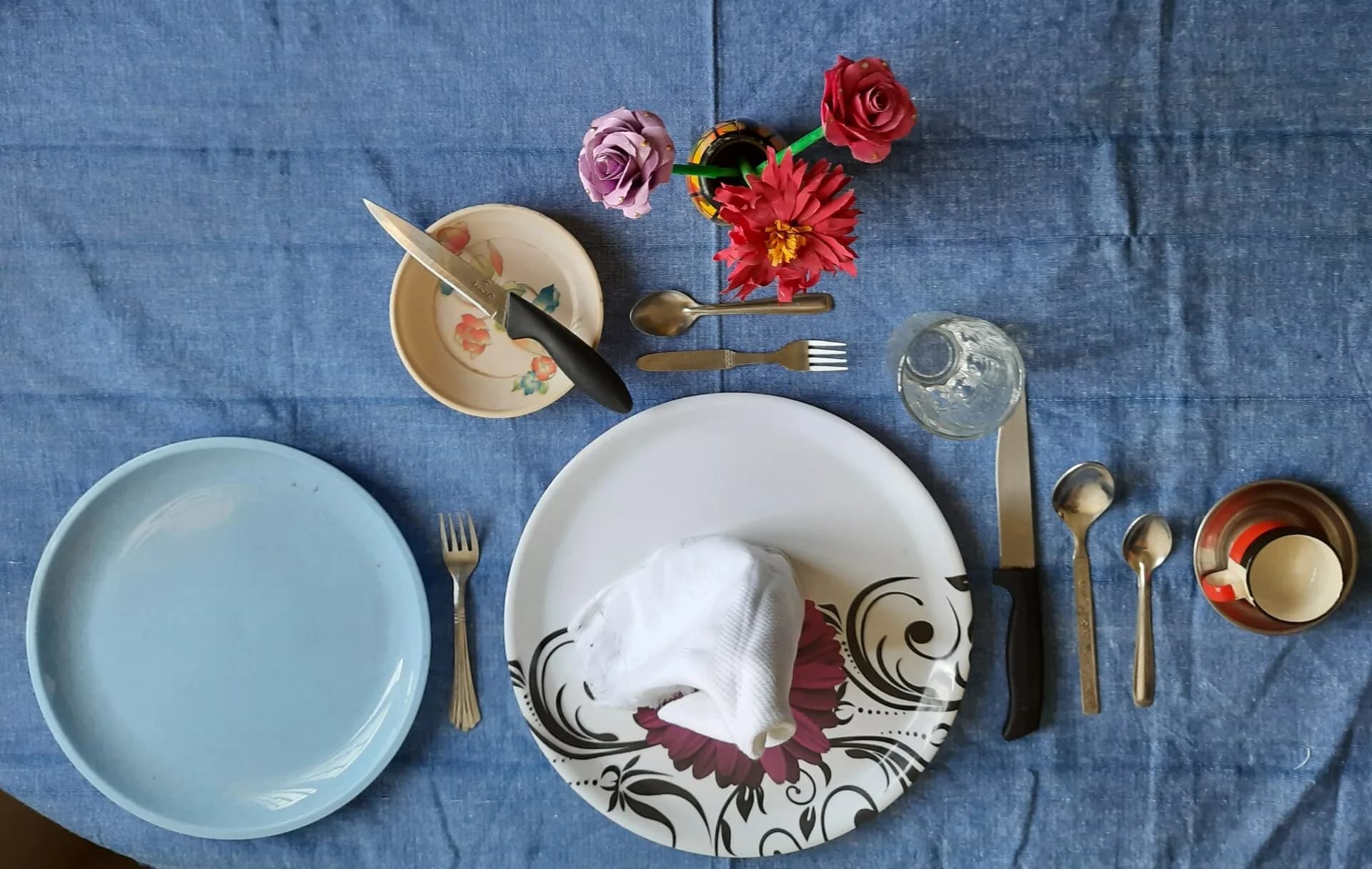 Mesa posta sobre toalha de mesa com pratos, talheres e copos