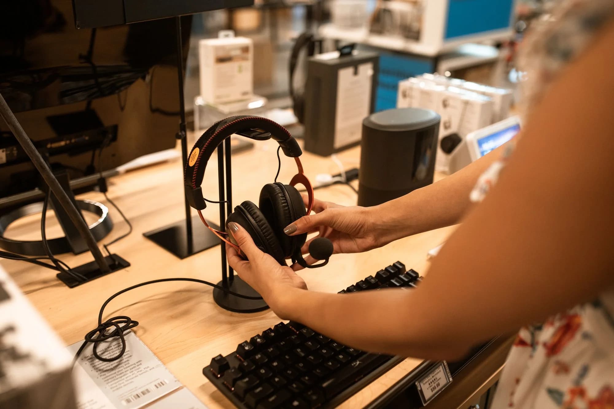 Cliente avaliando fones em uma bancada de loja de eletrônicos com teclado e caixas em exposição