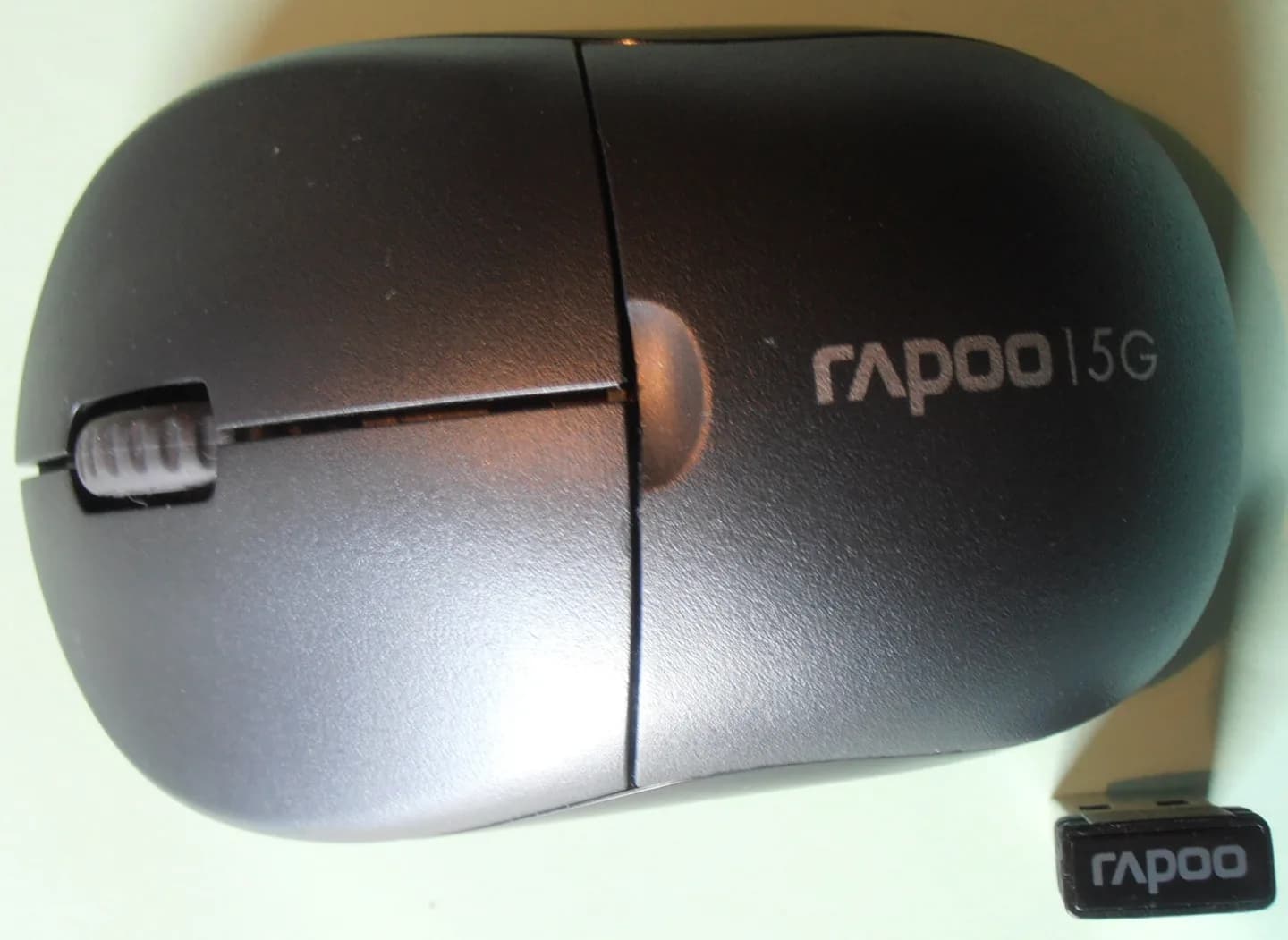 Mouse sem fio preto visto de cima com receptor USB ao lado