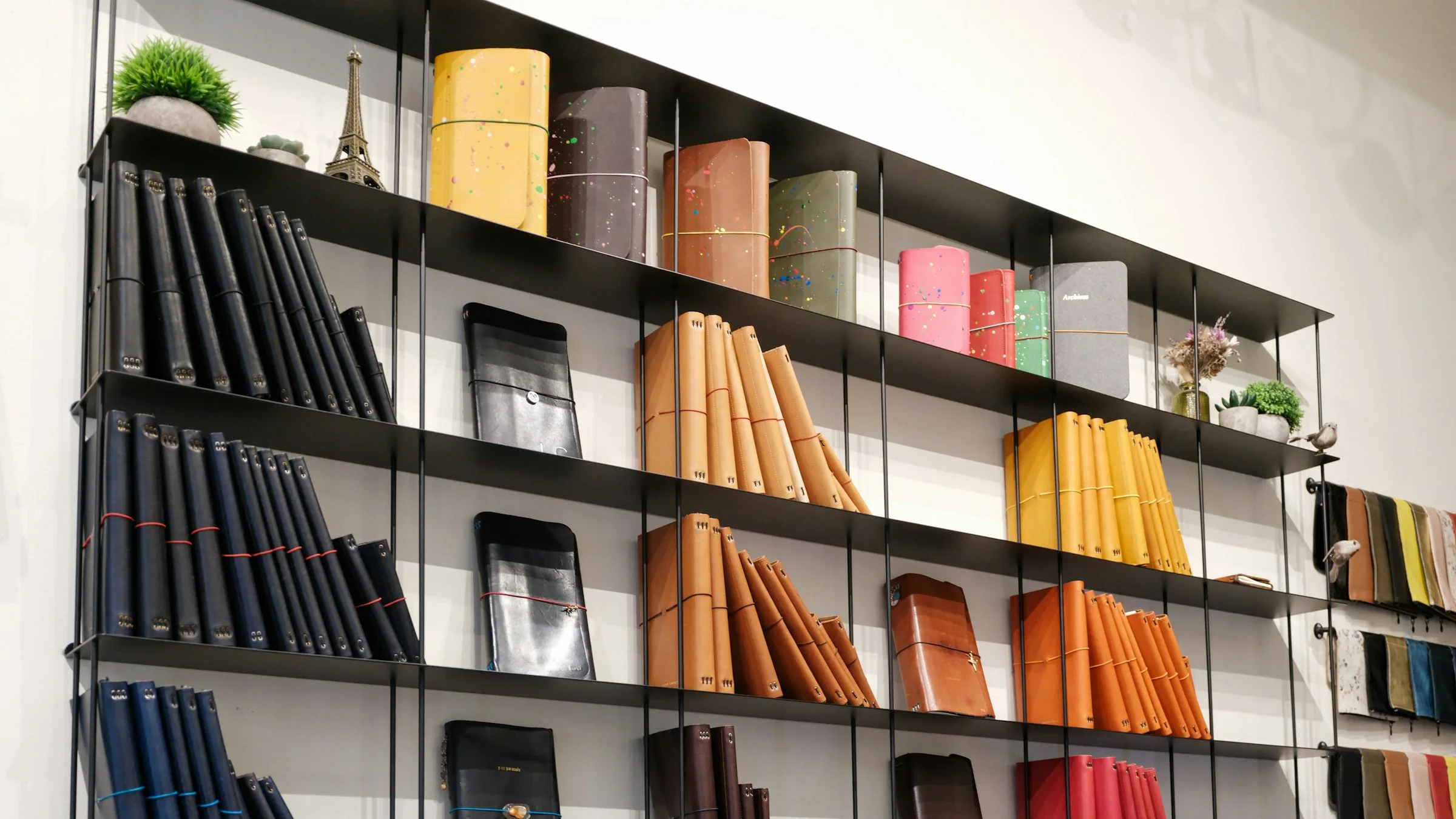 Prateleiras de papelaria com cadernos e diários neutros expostos por cor