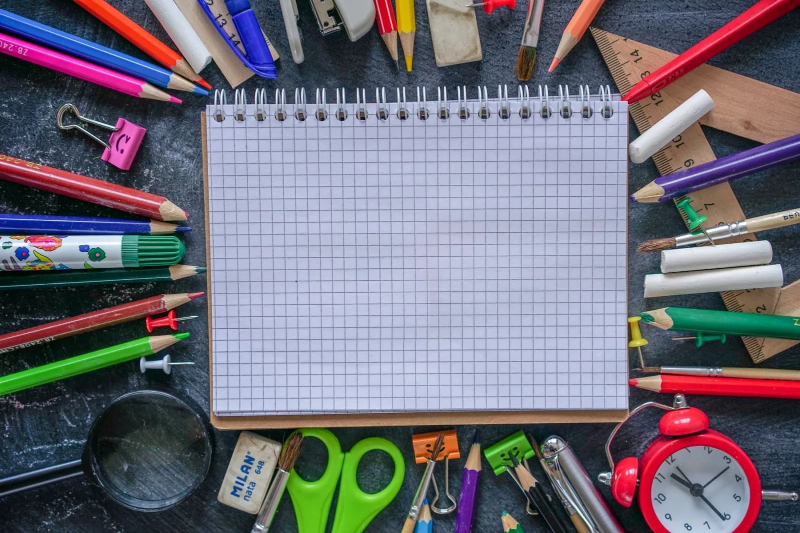Caderno quadriculado cercado por lápis, régua e outros materiais escolares