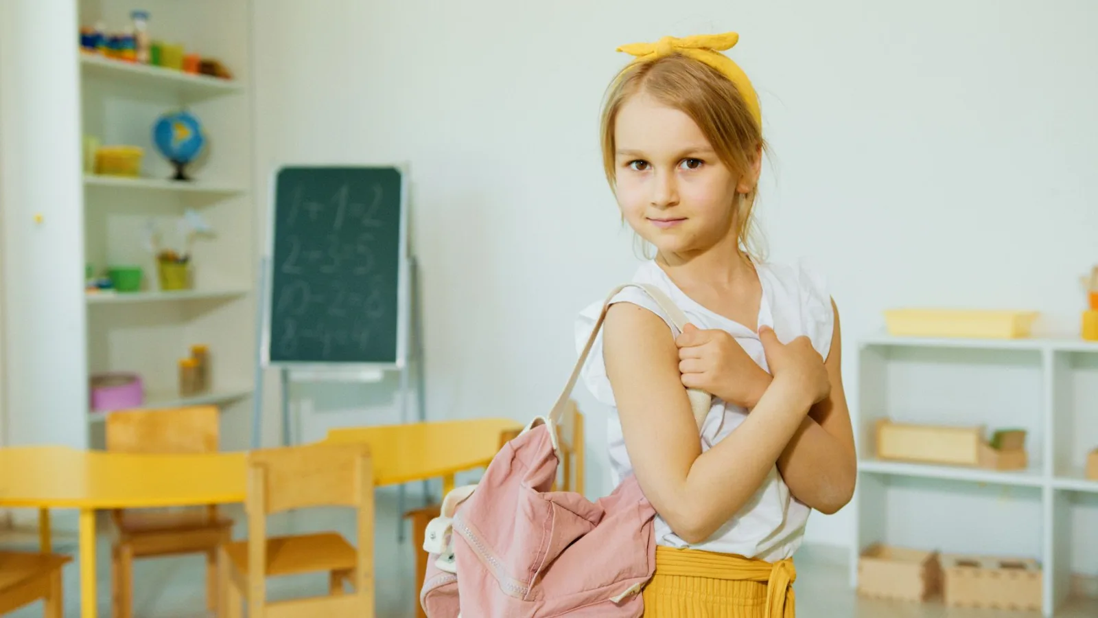 Estudante em sala de aula segurando uma mochila escolar rosa