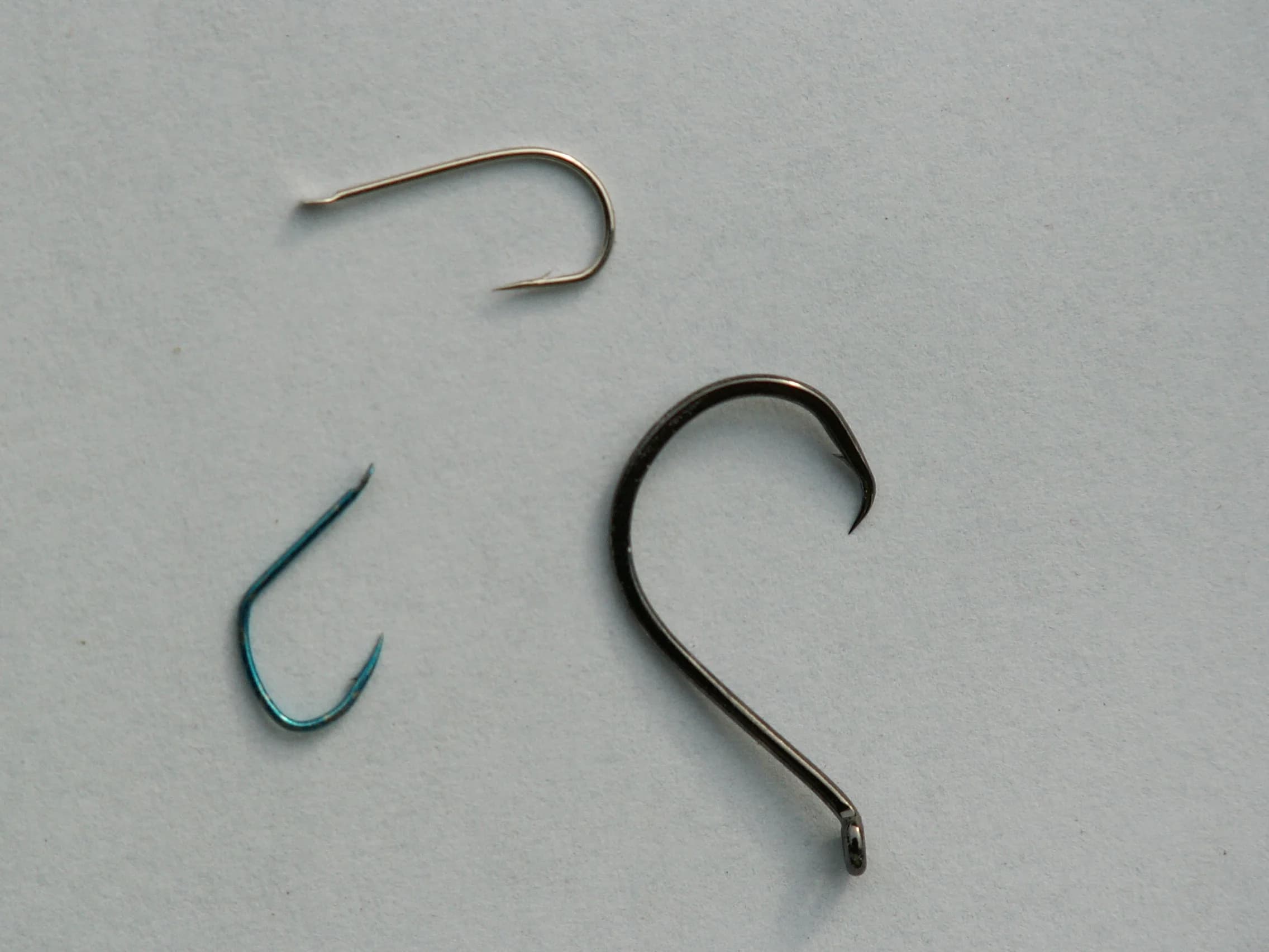 Três anzóis de pesca sobre uma superfície clara