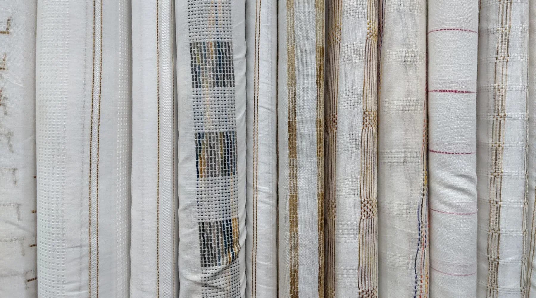 Exposição neutra de rolos de tecidos claros organizados lado a lado